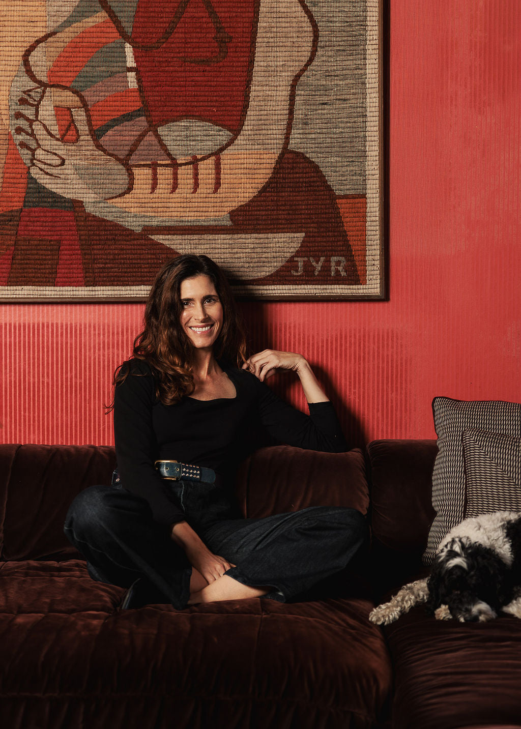 Woman sitting on a couch in front of a red wall with abstract art.